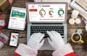 Santa working at festive table with cookies and tea on laptop dashboard showing overall productivity graphs. iPad showing Christmas countdown and staff time logs. iPhone showing map route and incoming messages.